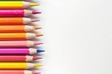 Fototapeta premium Colored pencils arranged in a neat row on the left side, with the pencil tips pointing towards the center of a white background. Horizontal photo with copy space.