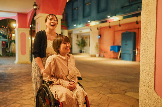 夜に車椅子に乗った日本人女性が友人と夏の沖縄旅行を楽しんでいる