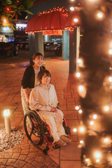 Obraz premium 夜に車椅子に乗った日本人女性が友人と夏の沖縄旅行を楽しんでいる