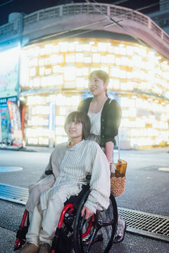 夜に車椅子に乗った日本人女性が友人と夏の沖縄旅行を楽しんでいる