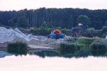 Machine extracting gravel from a gravel pit standing on the edge of the quarry at dusk.