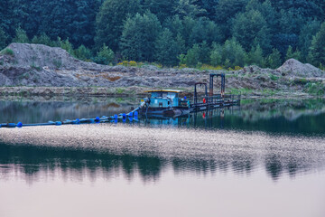 Machine extracting gravel from a gravel pit standing on the edge of the quarry at dusk.