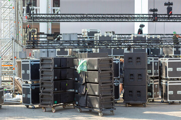 Stacks of sound equipment and lighting gear are arranged at an outdoor venue, ready for a concert.