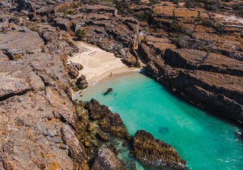 Aerial view of a serene turquoise lagoon surrounded by rugged rocky cliffs and a sandy beach.