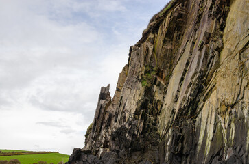 Sharp, vertical rock formations with a cloudy sky in the background in Wales.