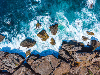 Waves of vivid turquoise slam into a rugged shore, with dramatic splashes and sea foam
