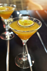 The martini glass with a yellow alcohol cocktail and a piece of maracuja is on the table in the bar. Close-up of a glass with cocktail Pornstar martini.