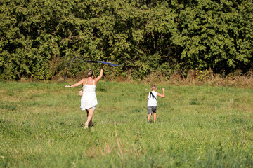 Woman with child running on a green meadow, flying a kite in park