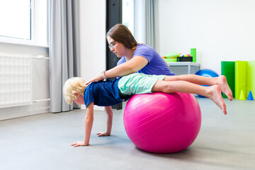 Young boy with female physical therapist exercising using ball during therapy session. Child...