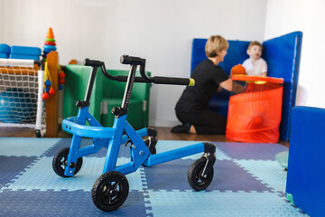 Children's walkers stand in rehabilitation room, in background a physiotherapist is doing...