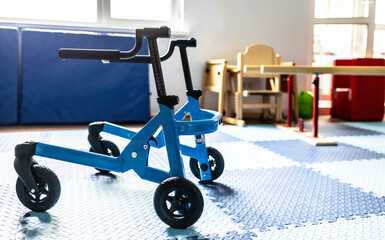 Blue walker mobility device is positioned in a therapy space designed for children's physical...