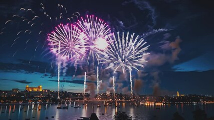 A dazzling display of colorful fireworks lights up the night sky above a bustling city skyline, reflecting beautifully on the water below. 