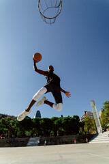 Street basketball player making a powerful slam dunk on the court - Athletic male training outdoor...