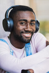 Young black unshaven man listens radio broadcasting online, uses headset, spends leisure time listening to music, has happy mood.