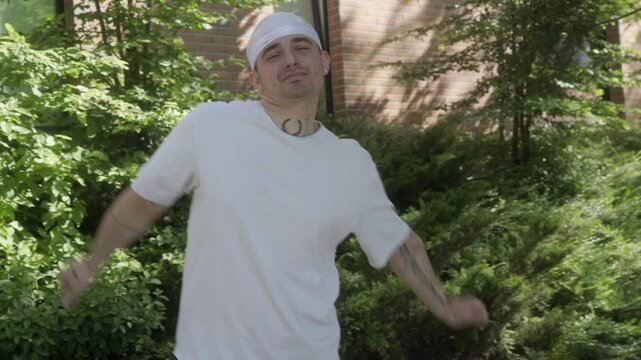A man in a white shirt and durag performs a modern dance, showcasing, carefree moves. Expressive gestures and dynamic energy highlight confidence, individuality, and a positive attitude.