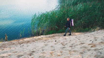 A Person Engaged in Climbing a Sandy Bank Right Next to the Water, Enjoying Nature. Hiking, young handsome male adventurer walking man through the forest with a big backpack. - Powered by Adobe