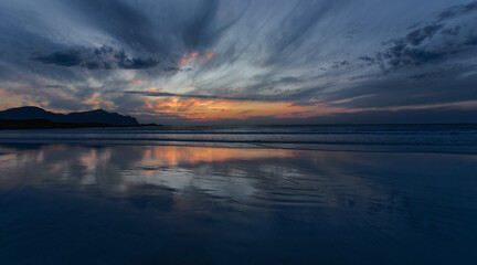 Naklejka premium Wide angle view of Sunset in cloudy sky over the calm sea. the reflection of the sunset on a pristine sandy beach. Lofoten Islands, Northern Norway.