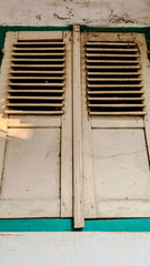 A pair of old, wooden window shutters painted in light beige with a teal frame.