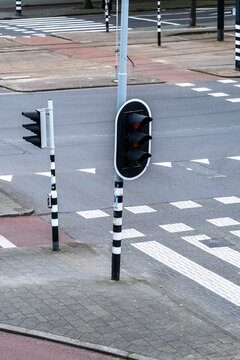 A traffic light at an empty urban intersection shows a red signal, with black and white striped poles and clearly marked crosswalks, viewed from above.