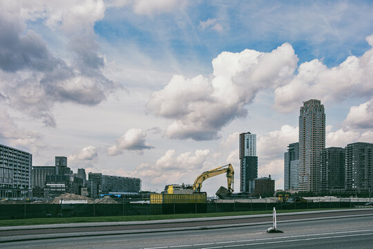 This image captures an active construction site featuring an excavator, with a modern city skyline in the background under a partly cloudy sky in Rotterdam
