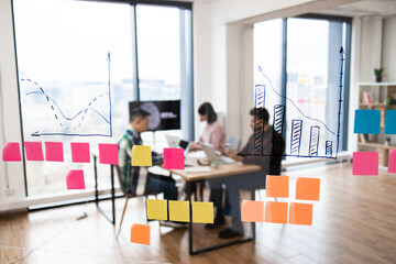 Group of IT experts working on developments in field of artificial intelligence. Brainstorming session with charts and sticky notes on glass wall in modern office environment.