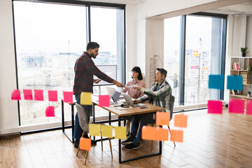 Group of coworkers collaborating in modern office with large windows, surrounded by colorful sticky notes. Active brainstorming session fostering creativity and teamwork.