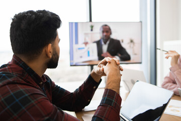 Professionals participating in business meeting via video conference call. Colleagues discussing project with laptop and screen sharing. Team collaboration in modern office setting.