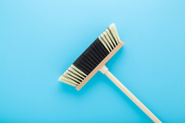 New white black broom with wooden stick on light blue table background. Pastel color. Closeup....