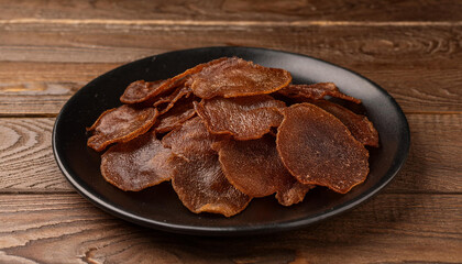 Fototapeta premium Dried beef and pork slices on plate, beer snacks or dog treats on wooden table. Tasty food.