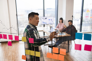 Business team in modern office having a meeting with a presentation on glass wall. Man presenting graphs and charts while colleagues participate in discussion.