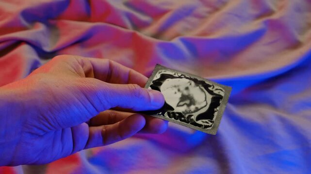 Hand holding a black condom wrapper with colorful fabric background, safe sex, intimacy.