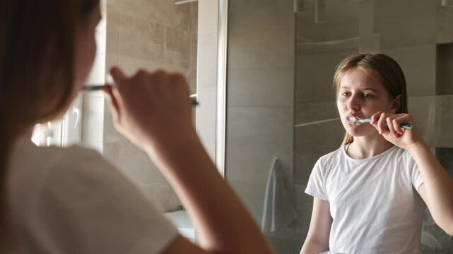 Little Girl Brushing Her Teeth In The Bathroom Mirror In The Morning