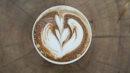 Cup of hot cappuccini with latte art on wooden table. Image in top view.