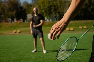 White badminton shuttlecock and badminton rackets in man hands. Summer sports outdoor activity. Game moment. Close up.