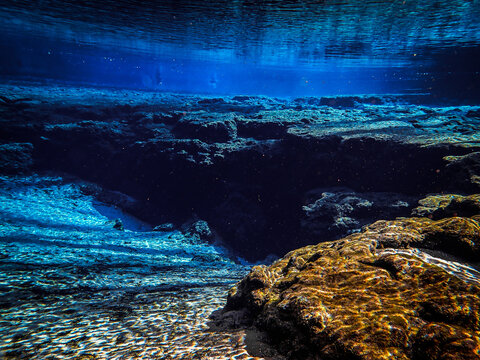 Blue waters of the spring basin drop down to the rocky cavern entrance at Ginnie Ballroom, Ginnie Springs, Florida