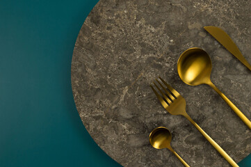 Top view of brown marble plate, gold cutlery on dark green background. Food presentation, stone...