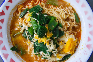 Close up delicious spicy noodle with vegetables and eggs served on white bowl isolated on gray background