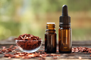 Two brown bottles of aromatherapy essential oil with red sandalwood chips in a bowl outdoors