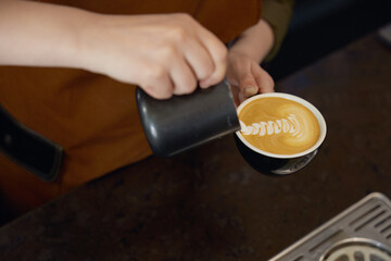 Closeup barista making latte art pouring steamed milk into ceramic cup
