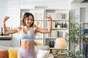 Young woman fitness and healthy lifestyle in her home, confidently flexing arm to show off her...