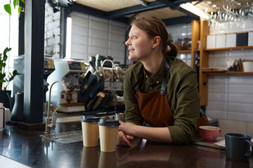 Portrait of dreamy female barista waiting for client with prepared coffee