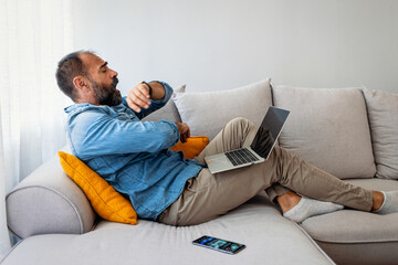 Man Relaxing on Sofa with Laptop and Smartphone Nearby