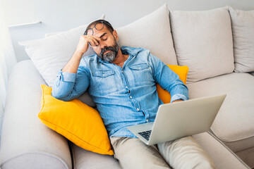 Exhausted Man Relaxing On Couch With Laptop At Home