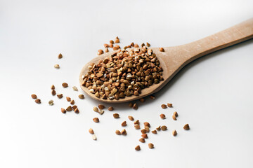Buckwheat in the wooden spoon with seeds on the white table.