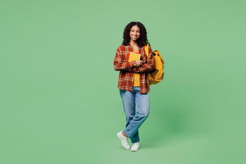 Full body young smiling happy fun teen girl student wear brown yellow casual clothes backpack bag hold books looking camera isolated on plain green background. High school university college concept.