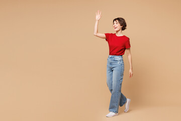 Full body side profile view young smiling happy woman wear red t-shirt casual clothes waving hand...