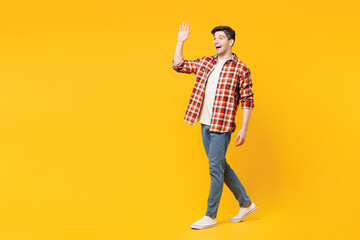 Full body side view young fun smiling cheerful happy man he wears red checkered shirt casual clothes walk go waving hand isolated on plain yellow orange background studio portrait. Lifestyle concept.