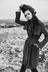 Mysterious woman in trench coat and boots standing on rocky beach