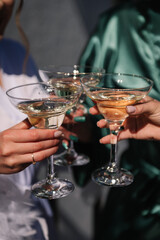 Cheers. Pretty young ladies friends wear silk robes hold glasses with champagne in hotel. Bride and bridesmaid celebrate bachelorette spa party. Closeup three female hands holding cocktails and drink.