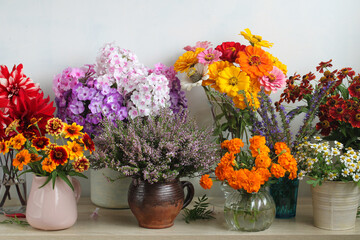 Fototapeta premium garden flowers in vases in a row on a shelf or table. a collection of different bouquets. a flower showcase. background, backdrop, texture.